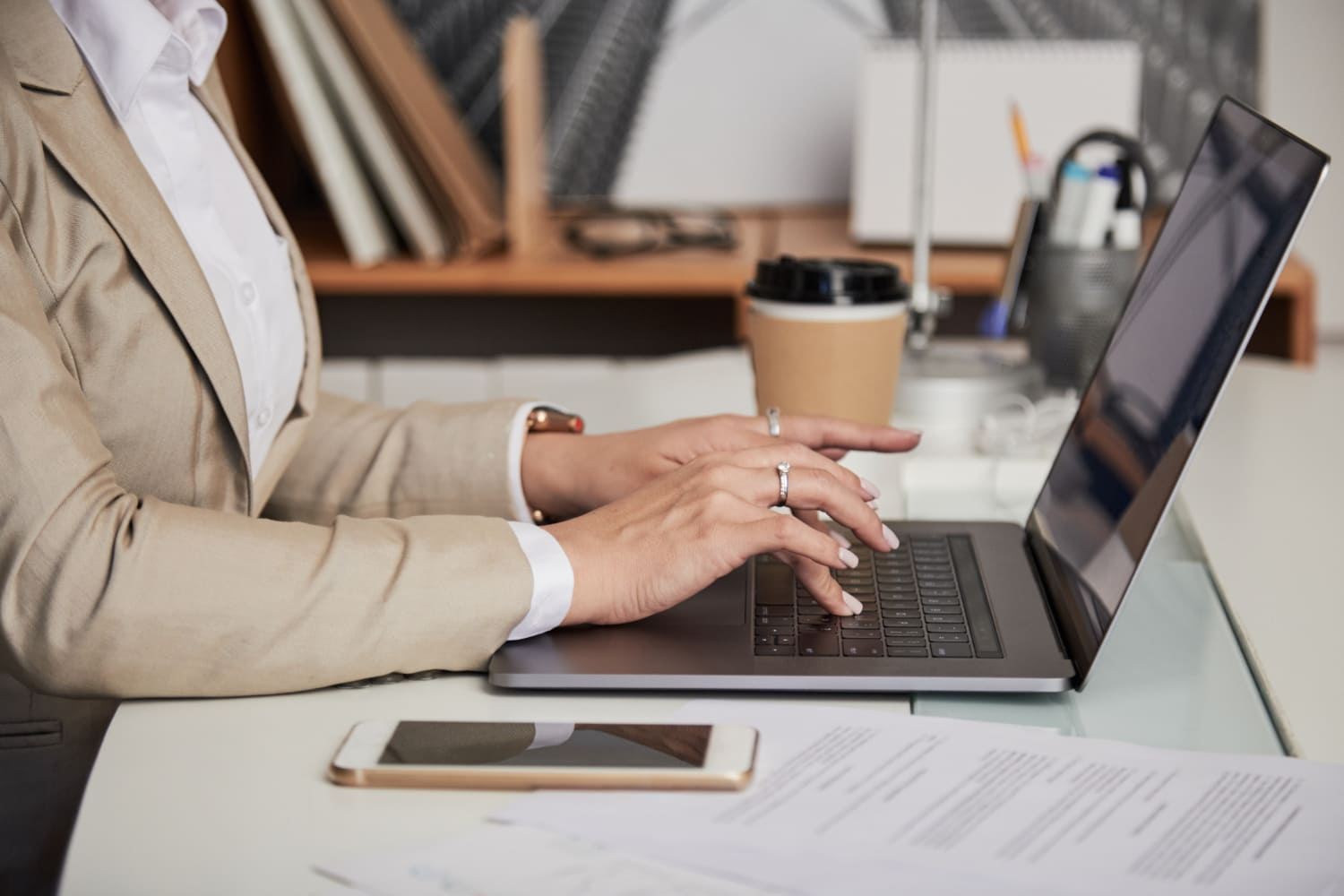 Professional typing on laptop with official documents on desk